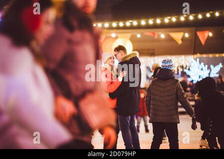 The theme is active recreation in winter on the ice arena. Young caucasian couple happy and in love glide together on an ice rink on christmas evening Stock Photo