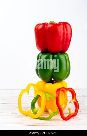 Red, green, yellow peppers whole and sliced and three wooden spoons with spices on wooden table. Stock Photo