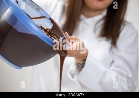 Closeup chocolatier pouring out of bowl dark melted hand-crafted chocolate Stock Photo