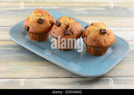Three banana chocolate chunk muffins in paper cups on blue serving platter Stock Photo