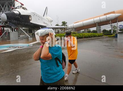 Visitors run for cover from the rain at the Kennedy Space Visitor Center Complex near Cape Canaveral, Florida in front of a mock-up of the space shuttle Explorer and a rocket booster July 7, 2011.  Space shuttle Atlantis, carrying a crew of four and food and other supplies critical for the International Space Station, is set to vault into orbit on Friday on the final flight in the 30-year U.S. shuttle program.  REUTERS/Hans Deryk   (UNITED STATES - Tags: SCI TECH)