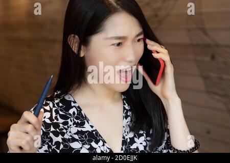 Very surprised Chinese American woman using an red smart phone in a coffee shop Stock Photo