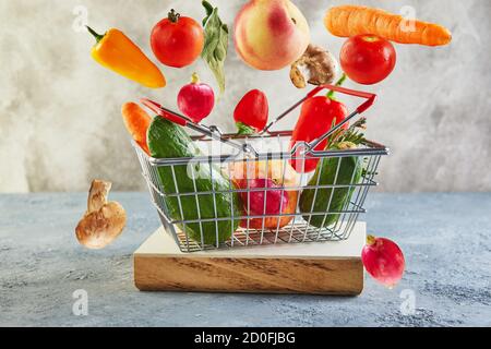 Various vegetables and fruits flying and falling into a supermarket basket standing on a wooden podium. Abundance and delivery concept. Stock Photo