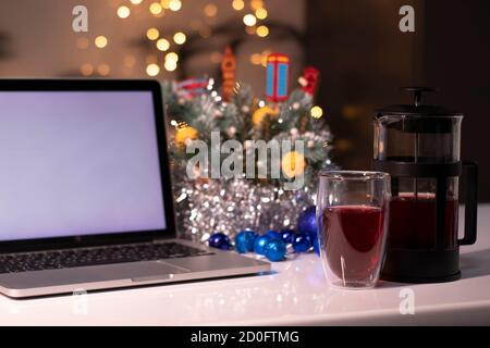 Laptop with white screen next to french press and tea near new years decorations. christmas theme template. Stock Photo