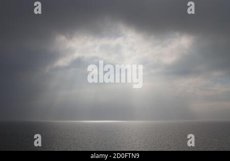 The sun breaks through the clouds above a misty, calm sea Stock Photo