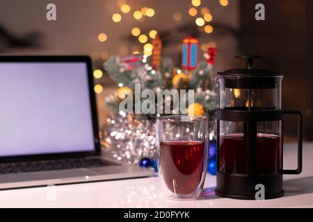 Laptop with white screen next to french press and tea near new years decorations. christmas theme template. Stock Photo