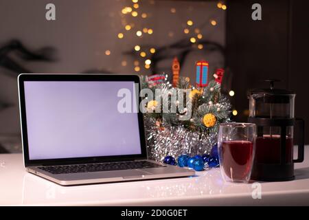 Laptop with white screen next to french press and tea near new years decorations. christmas theme template. Stock Photo