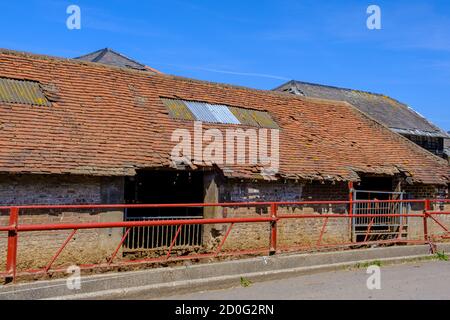 Old dilapidated farm building with broken red tiled roof & red metal fence in front. Pinner Park Farm, Pinner, Harrow, NW London UK. Stock Photo