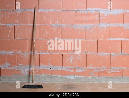 Old broom is leaning against a raw brick wall from Porotherm style clay blocks in a house under construction, architecture background with copy space Stock Photo