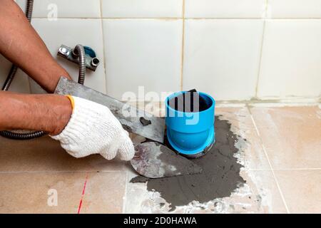 Construction workers are using plastering tools around the PVC pipe to drain the waste inside the bathroom. Stock Photo