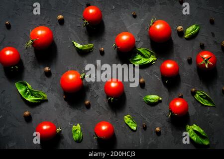 Fresh cherry tomatoes with basil leaves and black pepper on a black stone table, vegetable pattern, top view Stock Photo