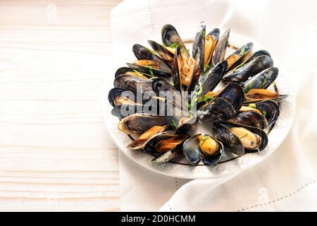 Fresh blue mussels with herbs served on a white plate on a bright wooden table, copy space, selected focus, narrow depth of field Stock Photo