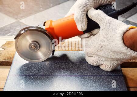 Construction worker wearing white cloth gloves was cutting the tiles with an electric grinder. Stock Photo