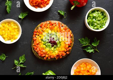Rainbow veggie bell peppers pizza on black stone background. Vegetarian vegan or healthy food concept. Gluten free diet dish. Top view, flat lay Stock Photo