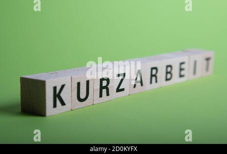 wooden blocks with german word for short time work, Kurzarbeit, green baclground