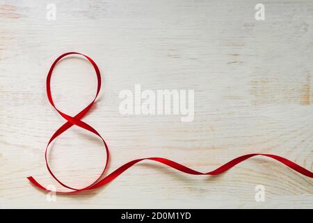 Red gift celebration ribbon waved in shape of number 8 (eight) on white wooden background. Greeting card with copy space for 8 March, International Wo Stock Photo