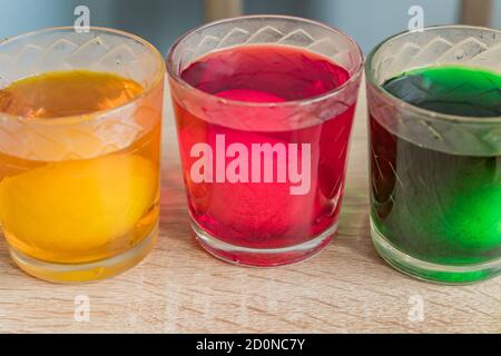 glasses with eggs in multicolored coloring water, close-up. Stock Photo