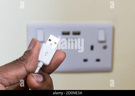 Man holding USB plug pin in front of two gang uk socket with USB ports Stock Photo