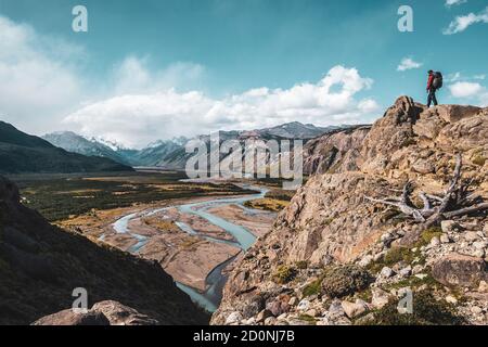 Hiker on top of a mountain admiring a valley with beautiful river in Patagonia.
