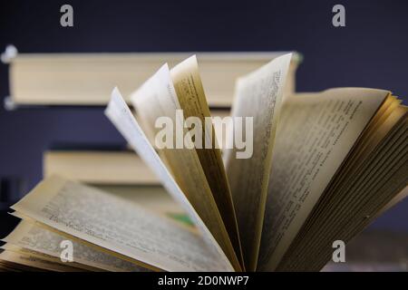 Close up of isolated open book hinge with flying pages, stack of blurred books background Stock Photo