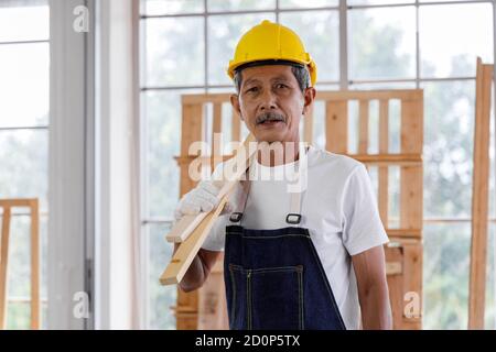 Portrait of Asian senior man with safety helmet working in carpentry workshop. Concept senior people doing hobby after retirement. Stock Photo