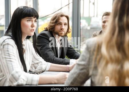 Meeting in progress. Two office workers are looking at their colleague with surpeise on their faces. Stock Photo