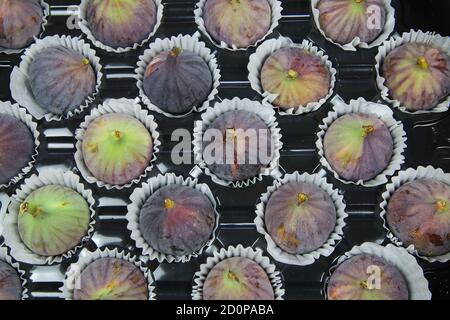 High angle view on isolated fresh ripe figs in paper cupcakes cups on black plastic tray Stock Photo