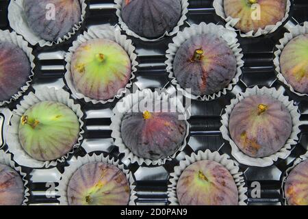 High angle view on isolated fresh ripe figs in paper cupcakes cups on black plastic tray Stock Photo