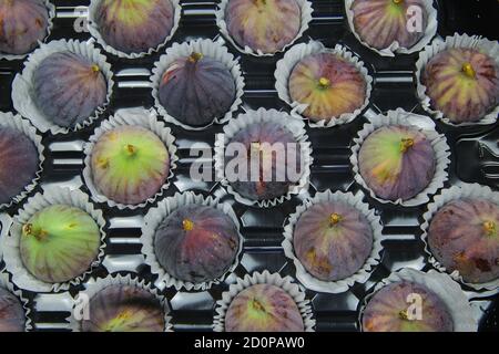 High angle view on isolated fresh ripe figs in paper cupcakes cups on black plastic tray Stock Photo