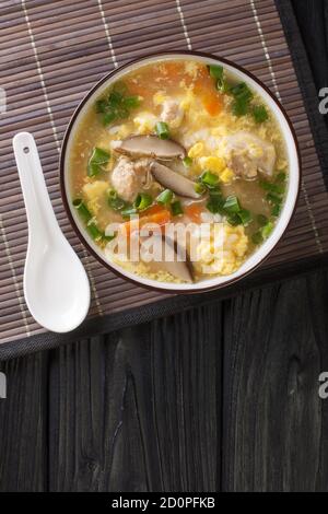 Japanese Zosui rice soup with egg, mushrooms, vegetables and chicken meat close-up in a bowl on the table. Vertical top view from above Stock Photo