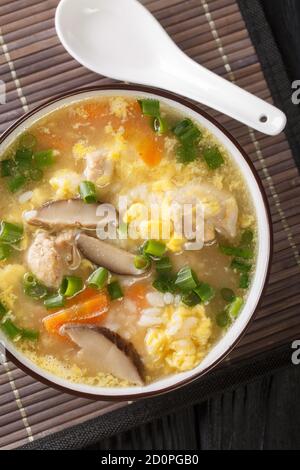 Zosui is a comforting Japanese rice soup cooked in a savory dashi broth with vegetables, eggs, mushrooms, and chicken close-up in a bowl on the table. Stock Photo