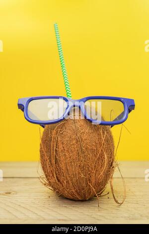 A coconut with green paper straw wearing 3D glasses on yellow background. Summer and trave concept Stock Photo