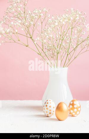 Happy Easter interior decoration. Three golden eggs and white blooming gypsoghila on pink background. Tender cozy still life. Stock Photo