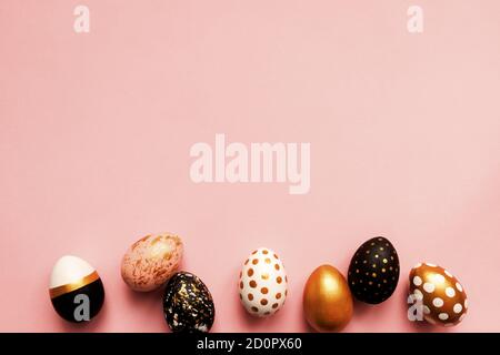 Frame made of wooden painted eggs in gold, black and rose colors on pink background. Happy easter background with copy space Stock Photo