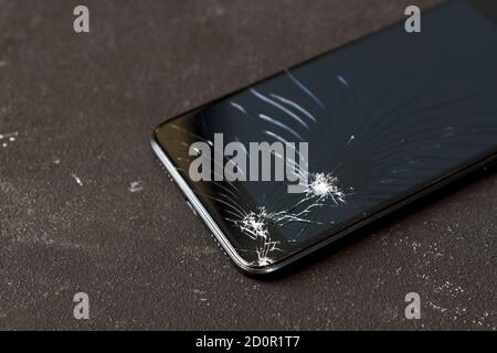 Broken glass of black smart phone on the dark background. Selective focus. Stock Photo