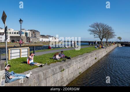 GALWAY CITY, IRELAND - 5th May, 2018: People enjoying a sunny spring day along the bank of Corrib river in the Claddagh area of Galway city, Ireland Stock Photo