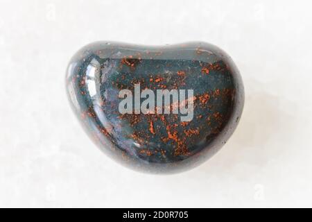 macro photography of sample of natural mineral from geological collection - tumbled Heliotrope (Bloodstone) gemstone on white marble background Stock Photo