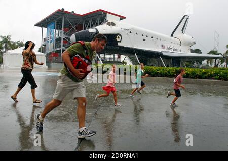 Visitors run for cover from the rain at the Kennedy Space Visitor Center Complex near Cape Canaveral, Florida July 7, 2011, in front of a mock-up of the space shuttle Explorer.  Space shuttle Atlantis, carrying a crew of four and food and other supplies critical for the International Space Station, is set to vault into orbit on Friday on the final flight in the 30-year U.S. shuttle program.  REUTERS/Hans Deryk   (UNITED STATES - Tags: SCI TECH)