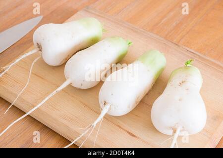Raw mooli radish (daikon) roots on a chopping board and kitchen table. Organic homegrown vegetables in UK Stock Photo