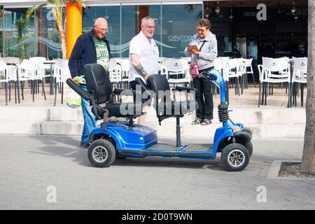 Benidorm, Spain - Holiday makers and disability scooter in Benidorm city nea outdoors cafe Stock Photo