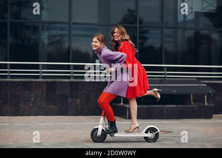 Two young women riding on electric scooter at the city Stock Photo