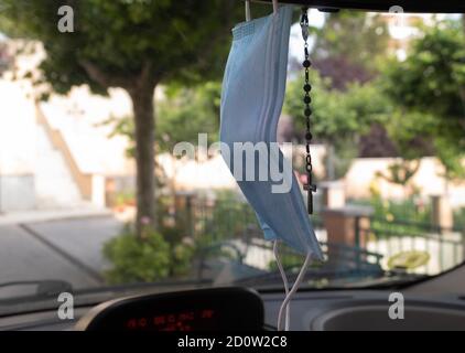 Sanitary mask and rosary hanging from the rear-view mirror of the car Stock Photo