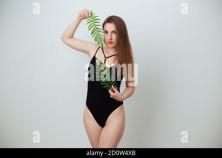 Model in a green swimsuit on an orange background holding a palm leaf Stock Photo