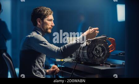 Professional Automotive Engineer in Glasses and Inspection Tools is Testing an Used Electric Engine in a High Tech Laboratory with a Concept Car Stock Photo