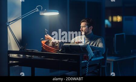 Professional Automotive Engineer in Glasses and Inspection Tools is Testing an Used Electric Engine in a High Tech Laboratory at Night. Stock Photo