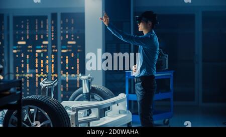 Automotive Engineer Working on Electric Car Chassis Platform, Using Augmented Reality Headset with Touching Gestures. In Innovation Laboratory Stock Photo