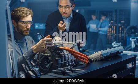 Two Professional Automotive Engineers with a Tablet Computer and Inspection Tools are Having a Conversation While Testing an Electric Engine in a High Stock Photo