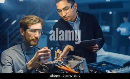 Two Professional Automotive Engineers with a Tablet Computer and Inspection Tools are Having a Conversation While Testing an Electric Engine in a High Stock Photo