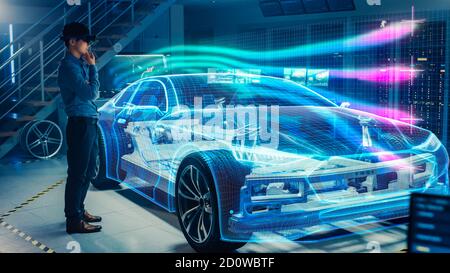 Engineer Wearing Augmented Reality Headset Working on New Electric Car Chassis Platform. 3D Graphics Visualization Virtual Model of a Vehicle is Stock Photo