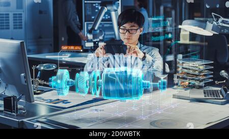 Industrial Engineer Works with Smartphone Using Augmented Reality Holographic Projection 3D Model of the Electric Generator Prototype. Development of Stock Photo